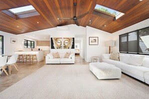 A spacious loft with a high ceiling, wooden beams, and skylights. It includes a living area with a sofa, a dining area with a table and chairs, and a kitchen with a central island.