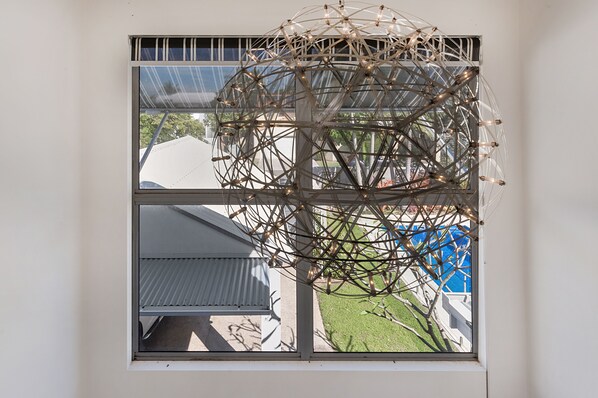 A window with a view of a spherical structure with lights, a building with a corrugated roof, and a blue pool.