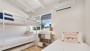 Ein Zimmer mit Etagenbetten, einem Schreibtisch, einer Lampe und einem Fenster mit Blick auf Palmen.