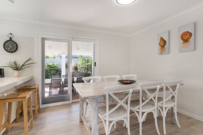 A dining area with a wooden table, white chairs, and a view through a glass door to an outdoor patio.
