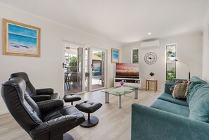 A modern living room with a leather sofa, a glass coffee table, a teal sofa, a TV, and a painting.