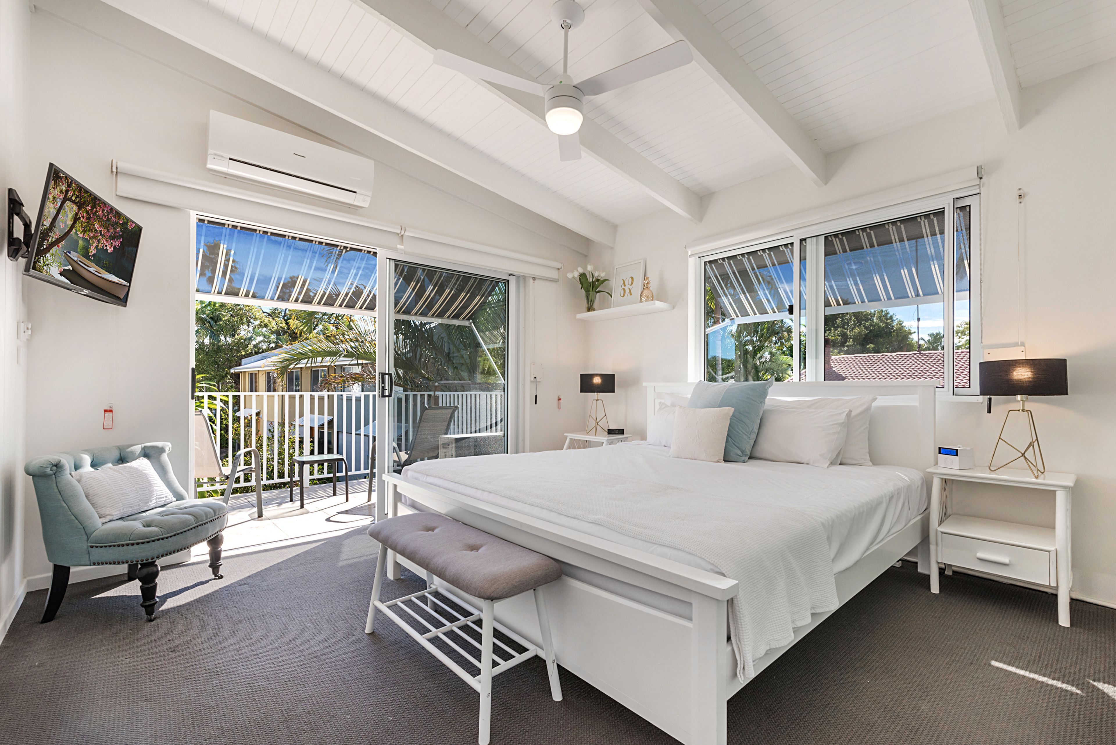 A bedroom with a large bed, a seating area with a chair and bench, a bedside table with a lamp, and a window with a view of the outdoors.