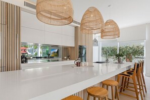 A modern kitchen with a large island, hanging rattan light fixtures, and wooden bar stools.