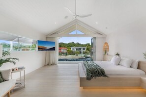 Une chambre moderne avec un grand lit, un ventilateur de plafond et une vue sur une maison et l’eau.