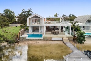 Une maison moderne à deux étages, dotée d’une piscine, d’un patio couvert et d’une terrasse en bois.