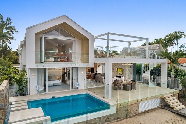 A modern two-story house with a glass-enclosed balcony, a swimming pool, and a staircase leading to the upper level.