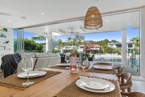 A dining area with a table set for four, a bottle of wine, and a view of a residential area with houses and greenery. - Key Court 17 (Noosa Heads)