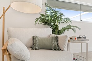 Un salon moderne avec un canapé, une lampe sur pied, une petite table avec des livres et une tasse, et une grande plante en pot.