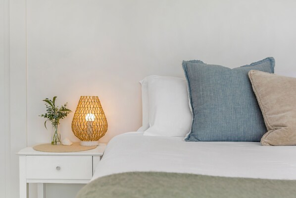 Un lit bien fait, avec des oreillers blancs et bleus, une table de chevet avec une lampe et une petite plante.