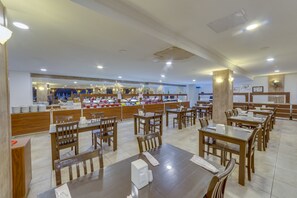 A restaurant with wooden tables and chairs, a buffet area with various food items, and a large mirror on the wall. - Smart Stay Beach Bodrum - All inclusive (Bodrum)