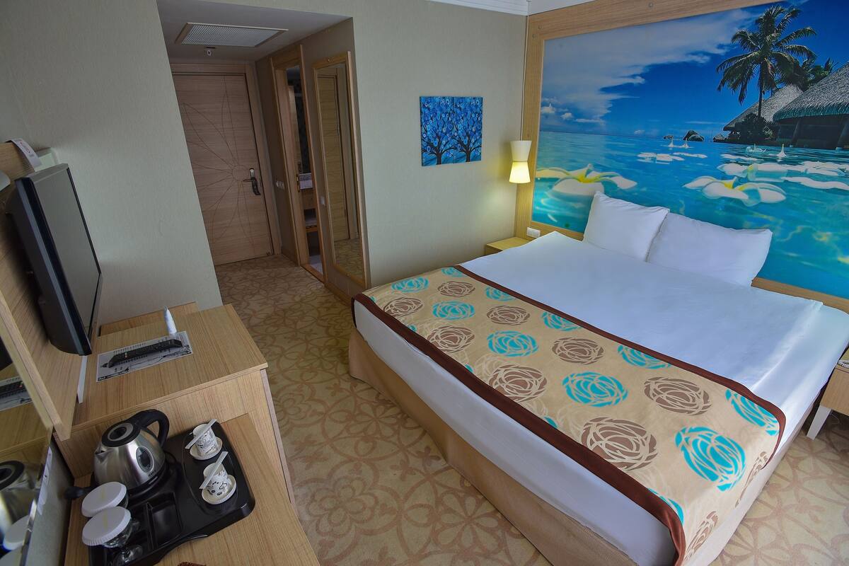 A hotel room with a bed, a TV, a desk with a kettle, cups, and a tray.
