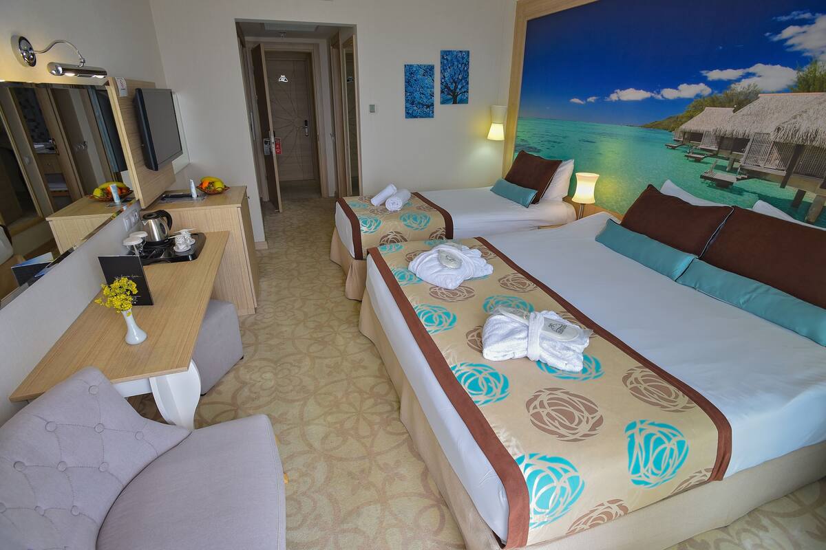 A hotel room with a bed, a desk with a computer, a chair, and a painting of a beach scene.