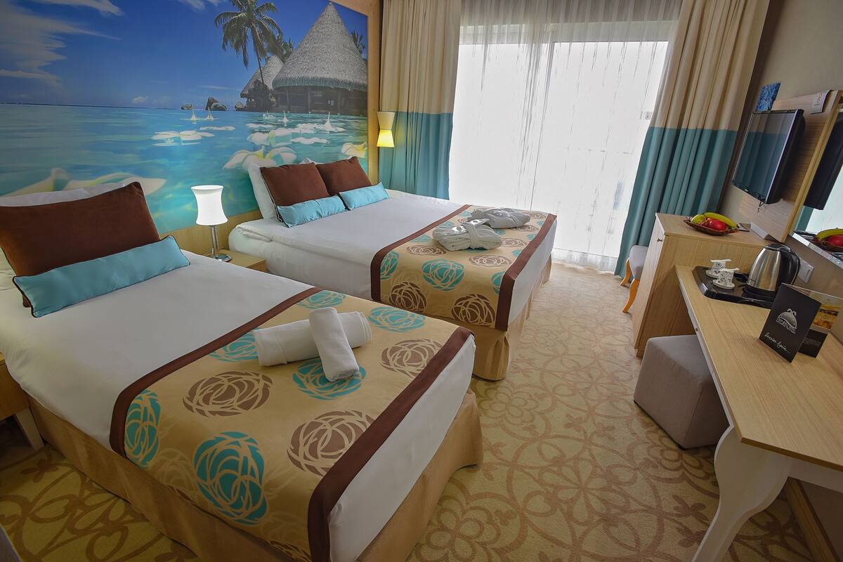 A hotel room with two beds, a desk, and a large window with curtains.
