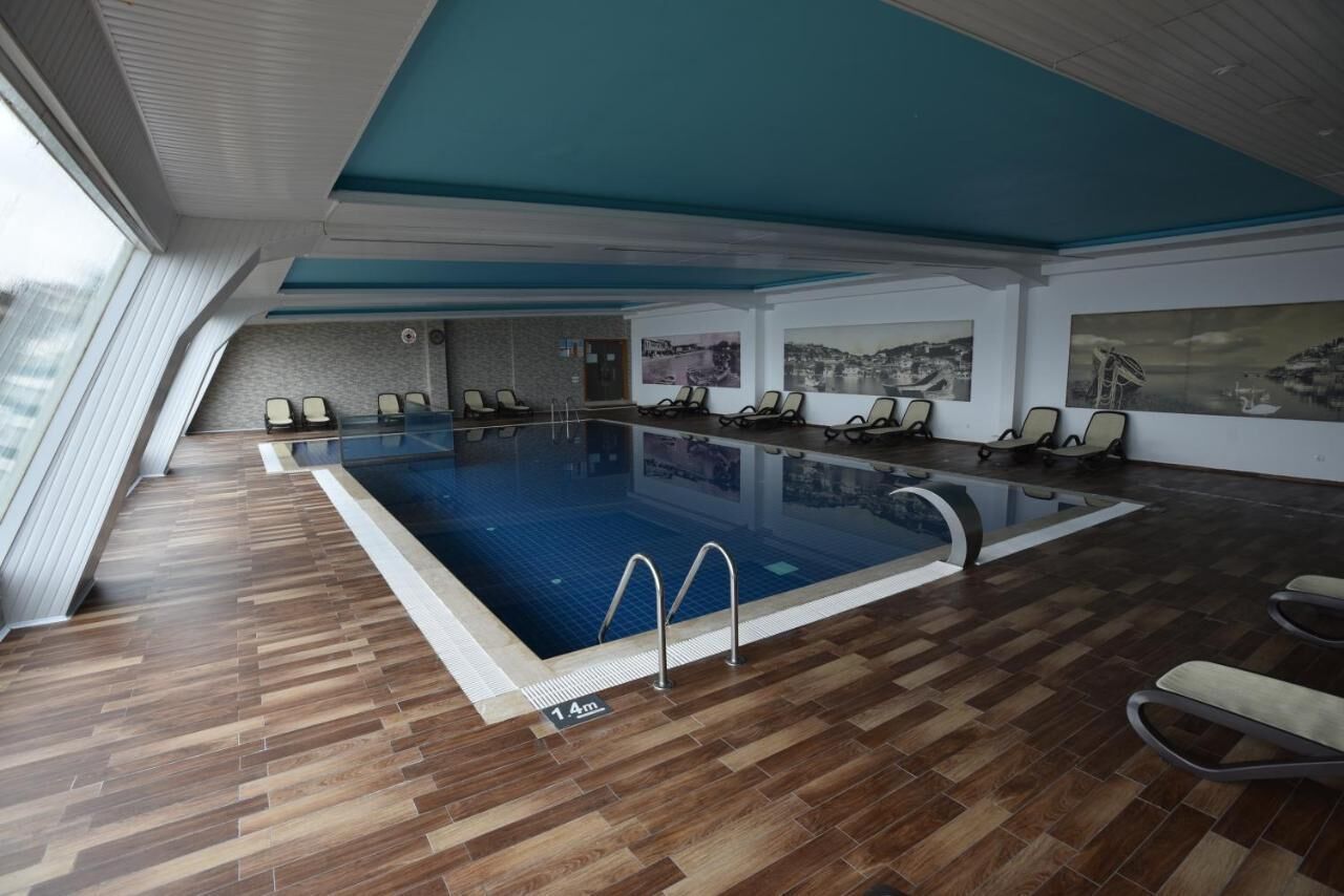 An indoor swimming pool with a wooden floor, lounge chairs, and wall art.