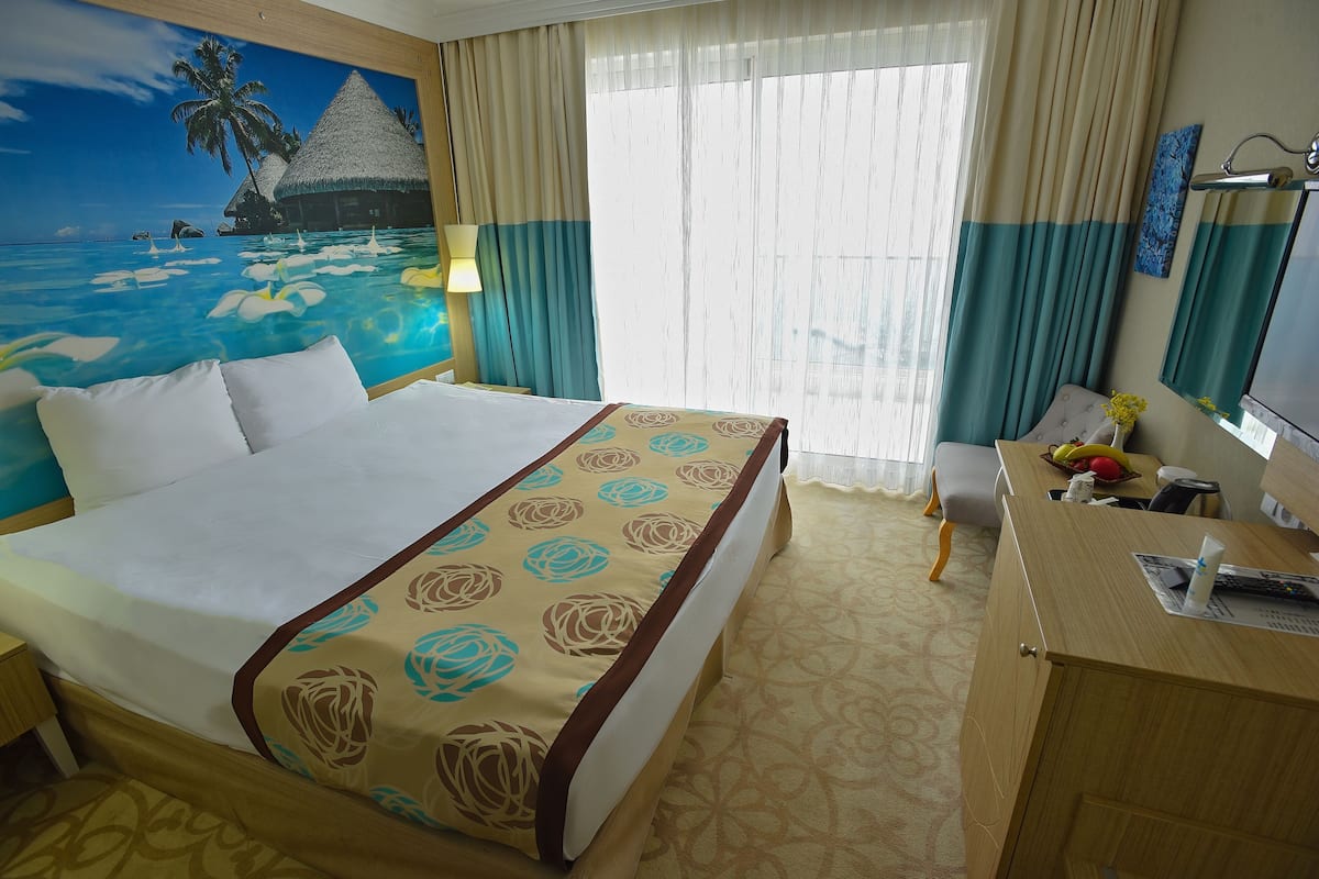 A hotel room with a bed, a desk, a chair, a lamp, and a large window with curtains.