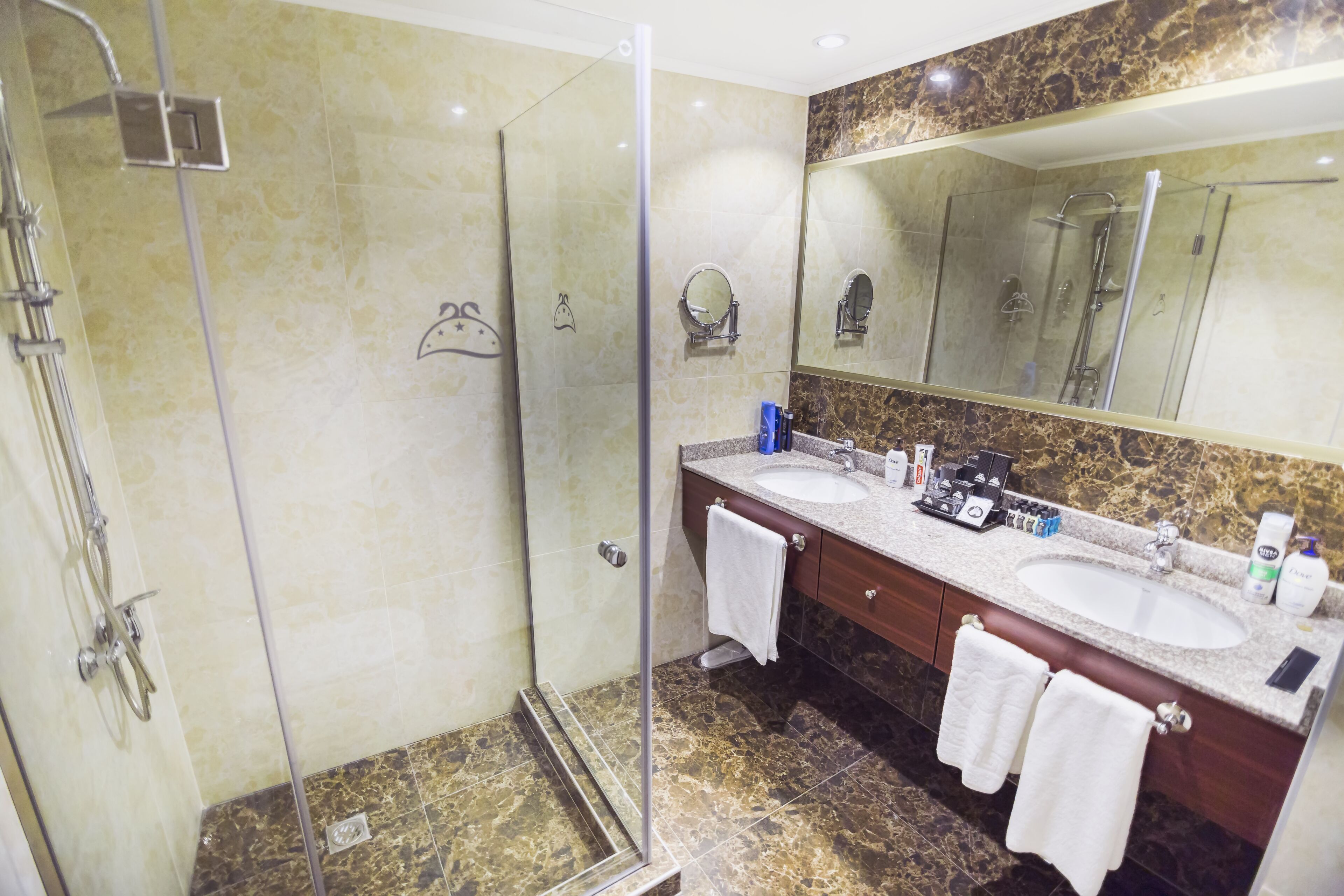 A bathroom with two sinks, a large mirror, and a glass-enclosed shower.