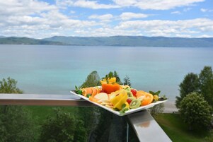 Un plato de fruta en un balcón con vistas a un lago y montañas al fondo.