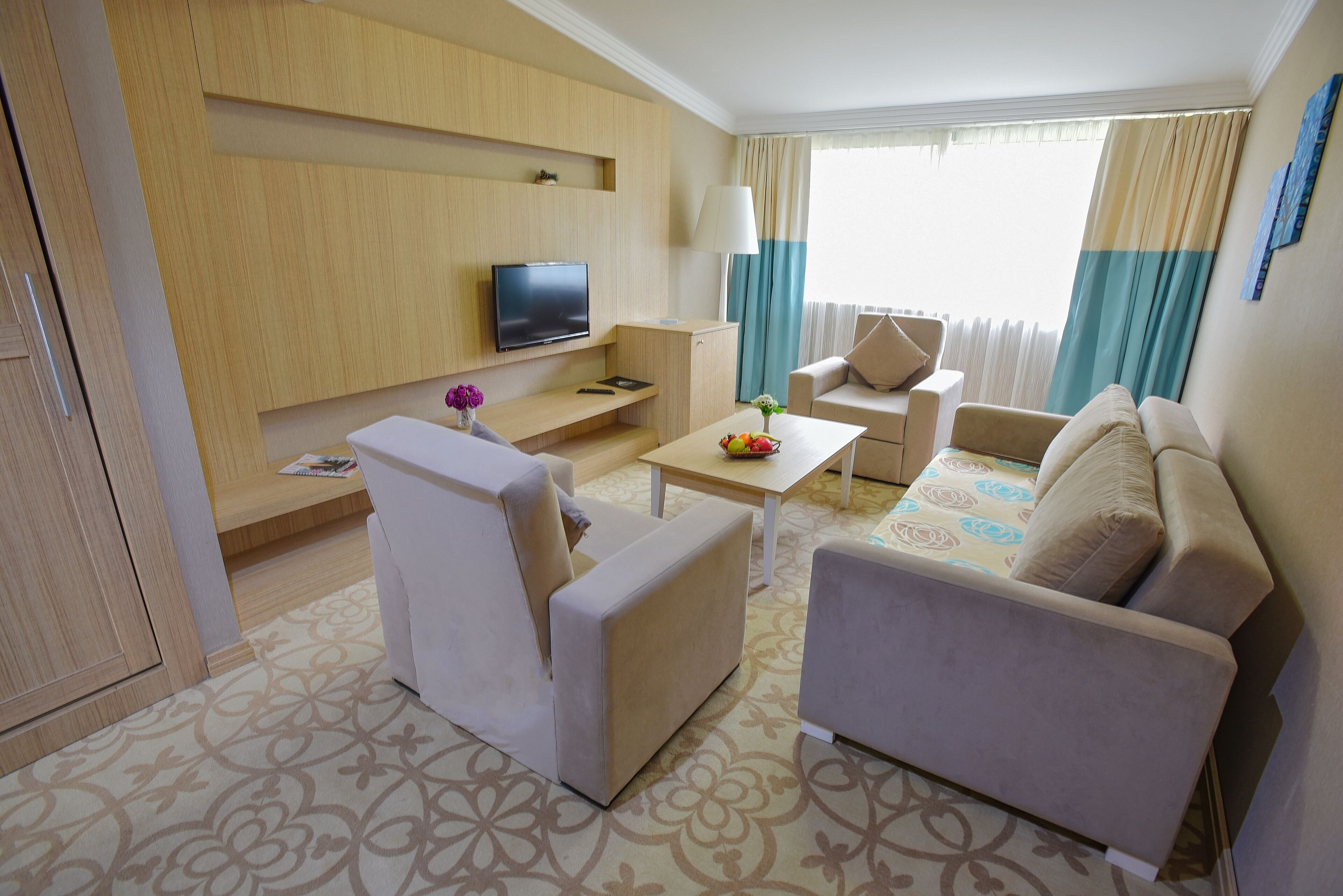 Habitación de hotel con televisión, sofá, sillón y una pequeña mesa con un florero.