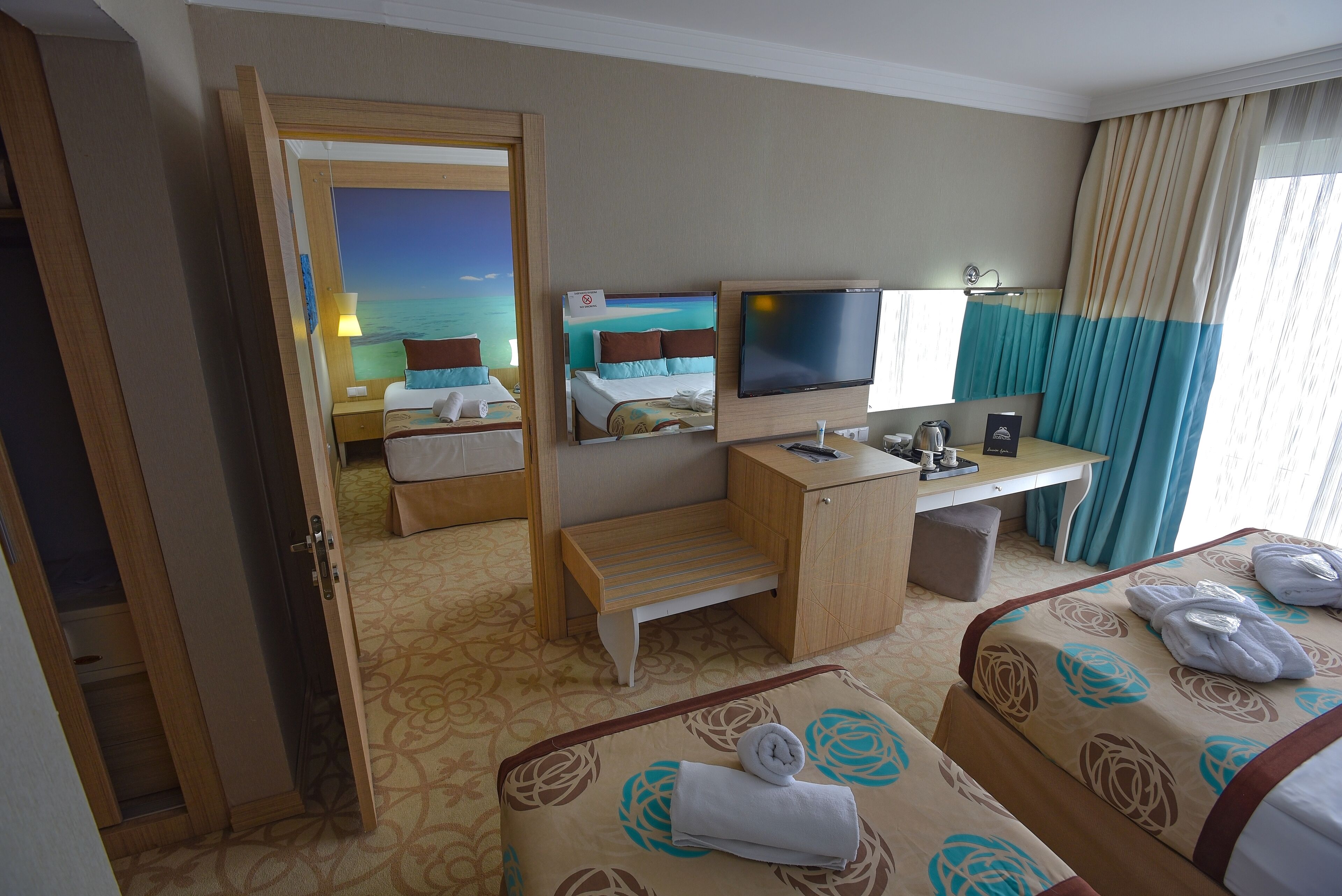 A hotel room with two beds, a desk, a television, and a view of the sea.