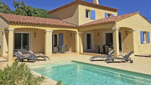 A two-story house with a swimming pool, outdoor seating, and a covered patio area.