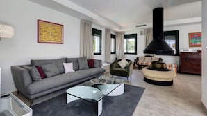 Una sala de estar moderna con sofá, sillón, mesa de centro de vidrio y chimenea.