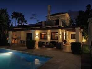 A two-story house with a swimming pool, outdoor seating, and a well-lit patio area.