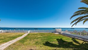 Ein grasbewachsenes Gelände mit weißem Zaun, einem Pfad und Blick auf das Meer.