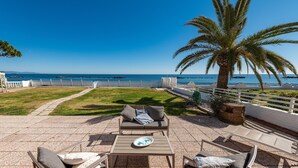 Eine Terrasse mit Gartenmöbeln, einer Palme und Blick aufs Meer.