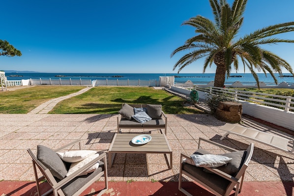 Une terrasse avec des meubles d’extérieur, un palmier et une vue sur la mer.