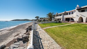 A coastal property with a stone pathway leading to a beach, a white fence, and a large building with multiple arches and a lawn. - Holiday Home "Nicoleup" with Sea View, Terrace & Shared Garden (Perd'e Sali)