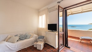 A room with a white sofa, a television, wicker baskets, and a view of the beach. - Holiday Home "Nicoleup" with Sea View, Terrace & Shared Garden (Perd'e Sali)