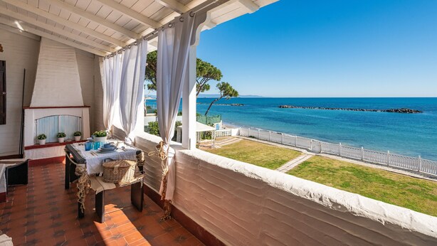 A terrace with a view of the sea, a table with outdoor dining setup, and a white railing. - Holiday Home "Nicoleup" with Sea View, Terrace & Shared Garden (Perd'e Sali)