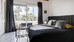 Un dormitorio con cama, ventana con cortinas, vista a palmeras y balcón.