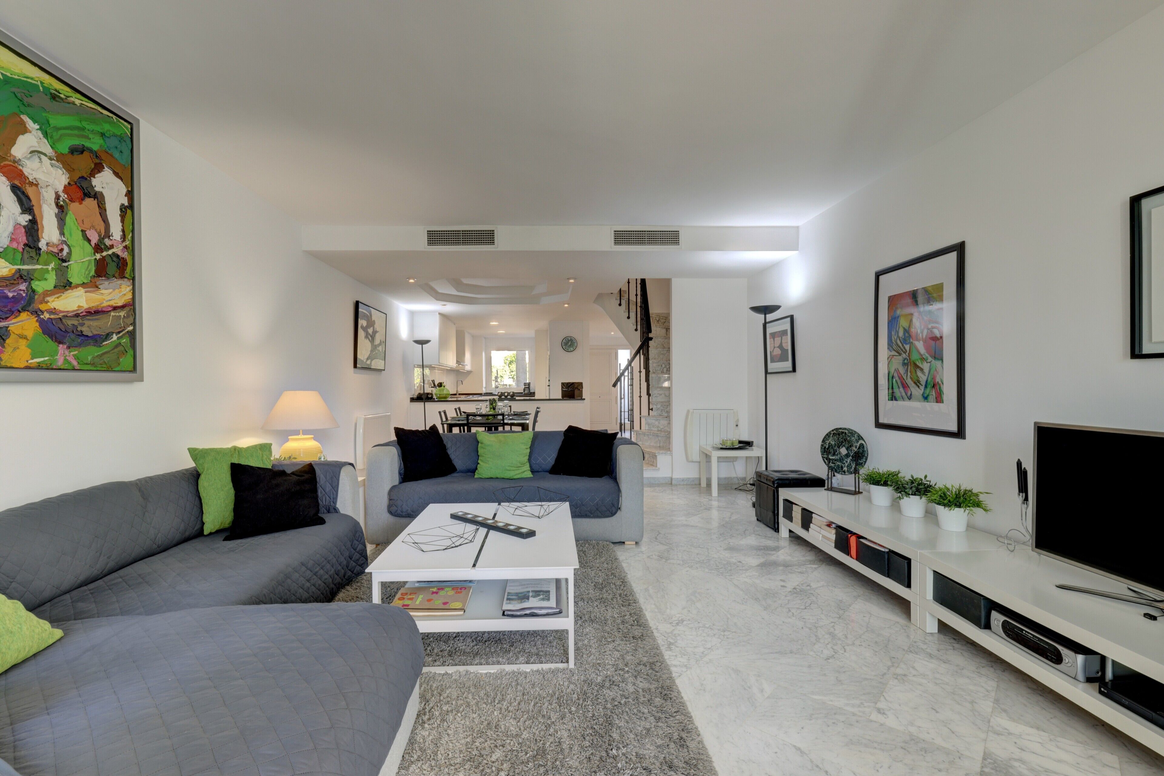 A modern living room with a grey sofa, a white coffee table, and a TV on a white stand.