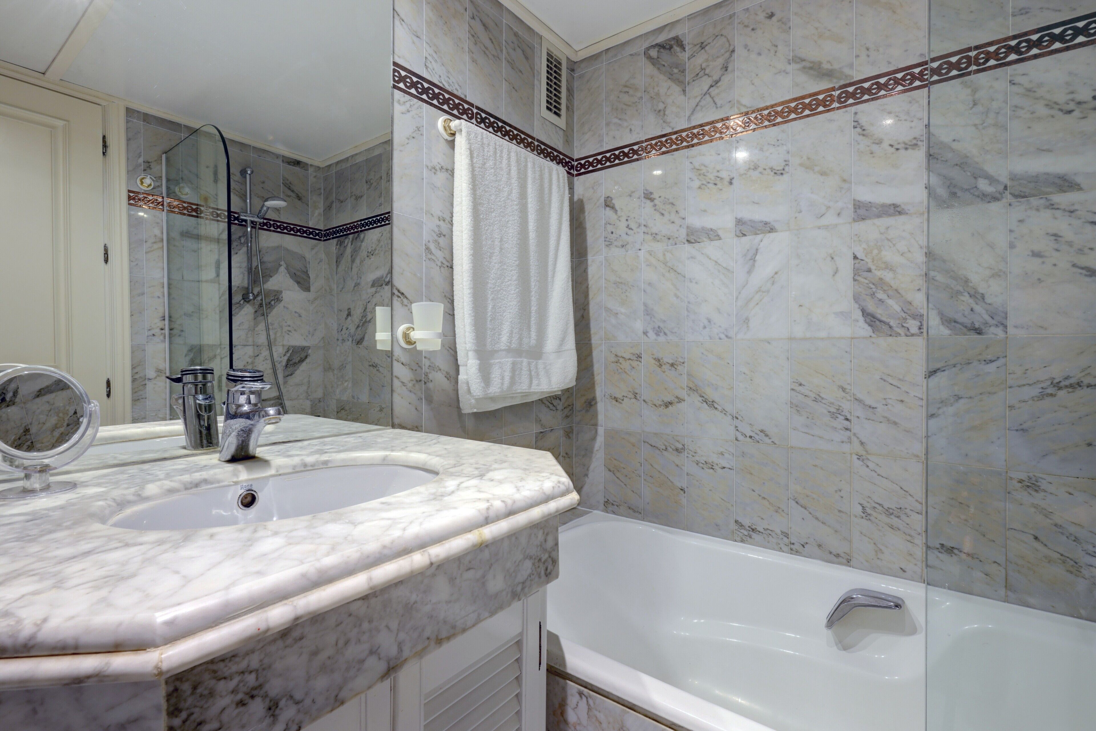 Un baño con lavamanos de mármol, bañera y ducha.
