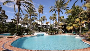 Una piscina con bordes de mosaicos, rodeada de palmeras y sillones de descanso.