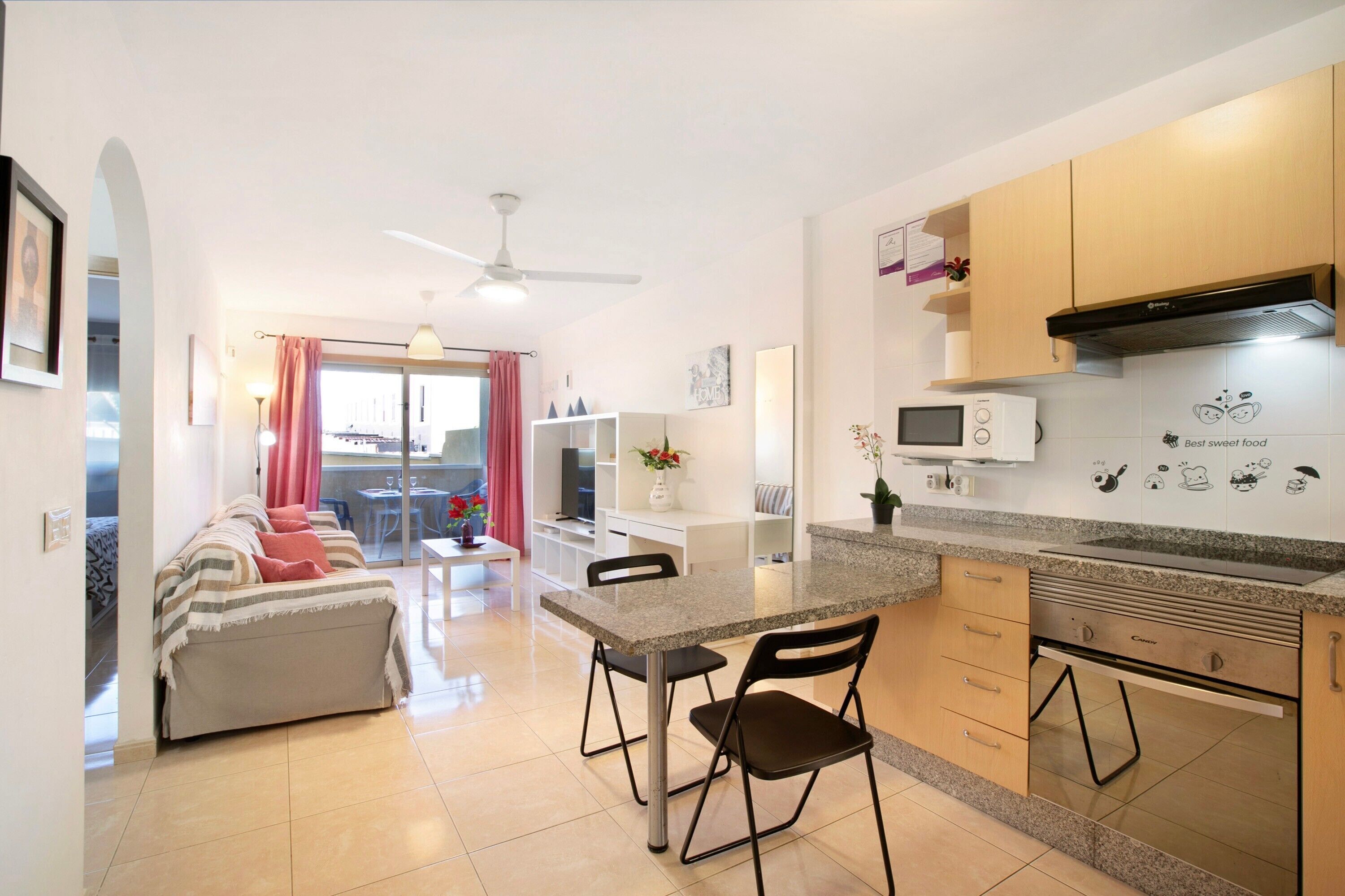 Une cuisine moderne avec un coin repas, un ventilateur de plafond et une vue sur l’extérieur grâce à une porte vitrée.