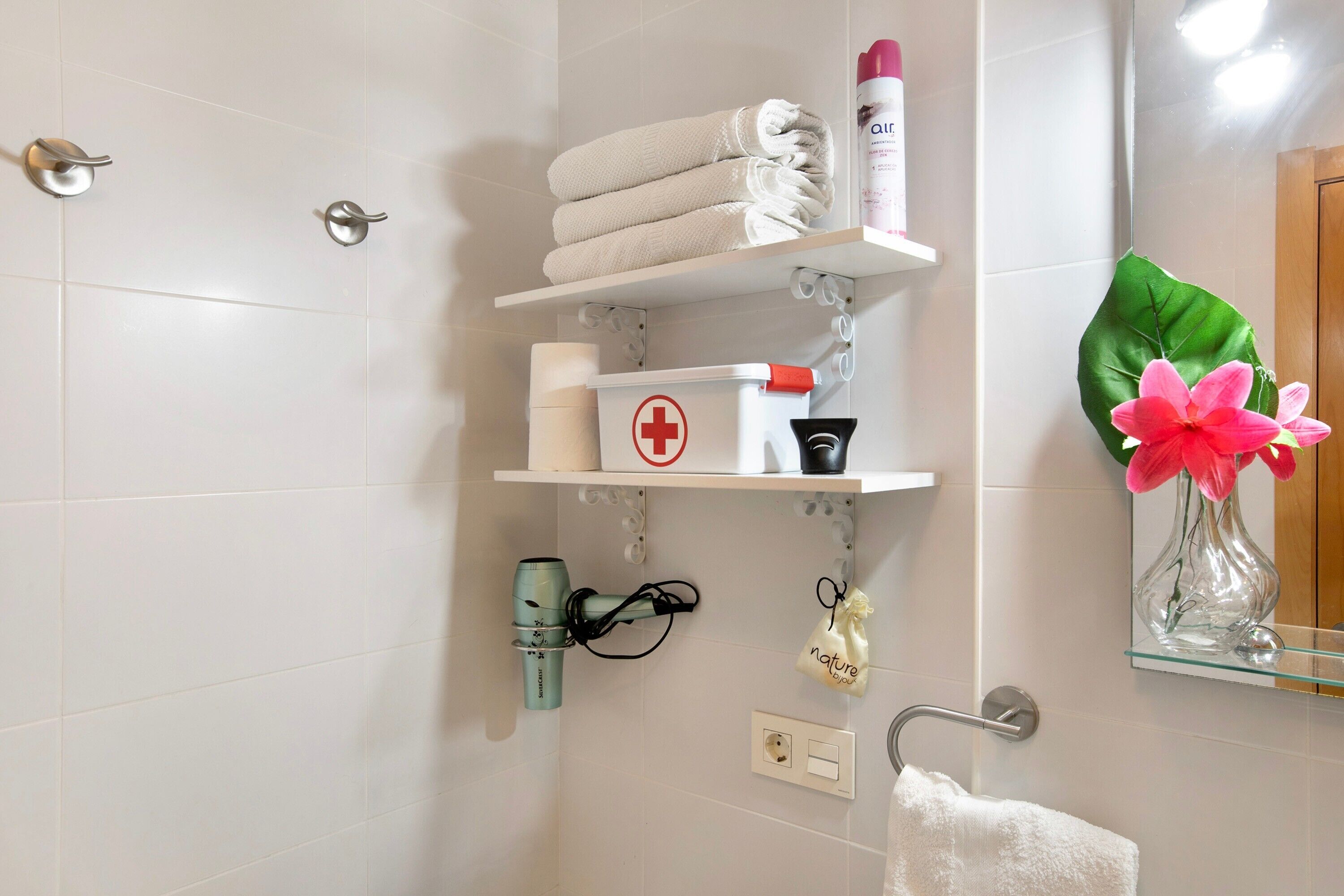 Ein Badezimmer mit weißem Handtuchhalter, Ablage für Toilettenartikel, Spiegel und einer Topfpflanze.