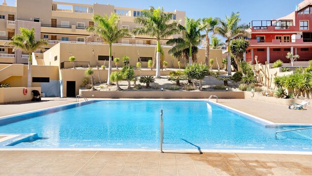 Una piscina con acqua cristallina e blu, circondata da palme e un edificio con balconi.