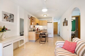 A modern kitchen with a dining area, a white desk, and a striped sofa.