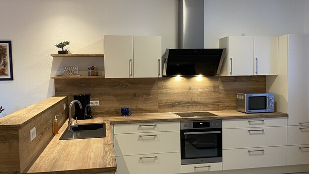 Una cocina moderna con armarios blancos, encimera de madera, horno empotrado, microondas y campana extractora de acero inoxidable.