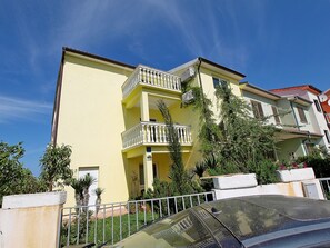 Um edifício amarelo de vários andares com varandas, um carro em primeiro plano e um céu azul límpido.