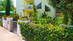 A two-story building with a yellow facade, a balcony with a white railing, and a small garden with various plants and flowers. - Apartment 56/34816 (Istria - Stinjan), 1000m from the beach (Stinjan)