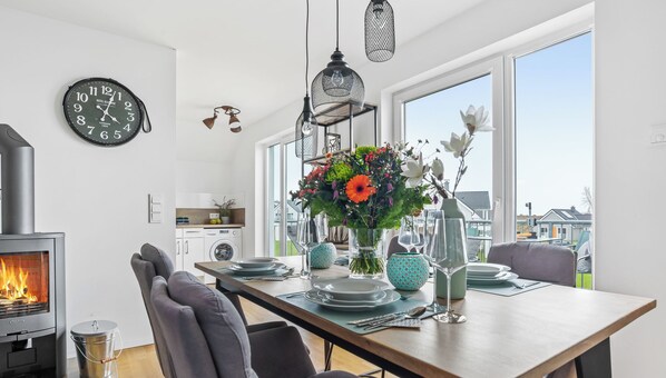 A modern kitchen with a wood-burning stove, a dining table set for four, and a large window offering a view of the neighborhood.