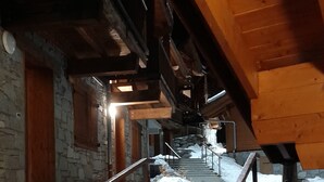 A staircase with metal railings leading up to a wooden ceiling. Snow is on the steps and the surrounding floor.