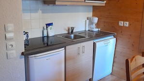 A compact kitchen with wooden cabinets, a microwave, a small refrigerator, and a coffee maker.