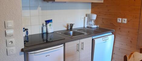 Een kleine keuken met houten kastjes, een magnetron, een koffiezetapparaat en een kleine koelkast.