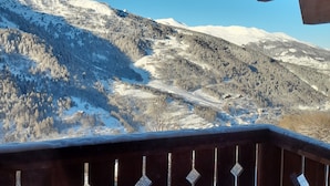 A wooden balcony with a view of snow-covered mountains and a clear sky.