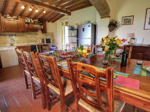 A dining area with wooden chairs and a table set for a meal, a refrigerator, and kitchen cabinets.