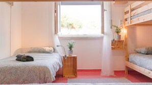 A cozy bedroom with a bunk bed, a small bedside table with a plant, and a window providing natural light.